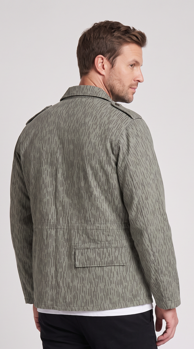 A man wearing a textured sage green jacket, shown from the back, paired with black trousers, against a light gray studio background.