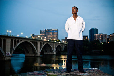 Man wearing vintage 1970s HBT Navy Style middy shirt with button-up cuffs standing by city river at dusk