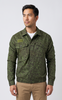 A man wearing a green camouflage long-sleeve button-up shirt over a white undershirt and khaki pants, standing against a light gray studio background.