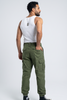 A man shown from the back wearing olive green cargo pants, a white tank top, and black sneakers against a light gray studio background.