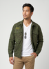 A man wearing a green camouflage button-up shirt jacket over a white t-shirt and khaki pants, standing against a light gray studio background.