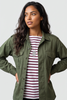 A woman wearing an olive green military-style button-up shirt over a red and white striped t-shirt, photographed against a solid light gray background.