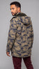 A man wearing a hooded camouflage jacket in tan and navy blue, shown from a three-quarters back view against a solid gray studio background.