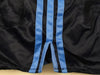 Adidas shorts Close-up of a black satin-like garment with two vertical light blue stripes down the center, laid flat on a pale beige surface.