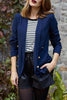 Woman wearing a navy blazer over a striped shirt with a stone wall background