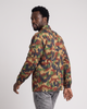 A man wearing a camouflage utility jacket and gray jeans, shown from a side-back angle against a light gray studio background.